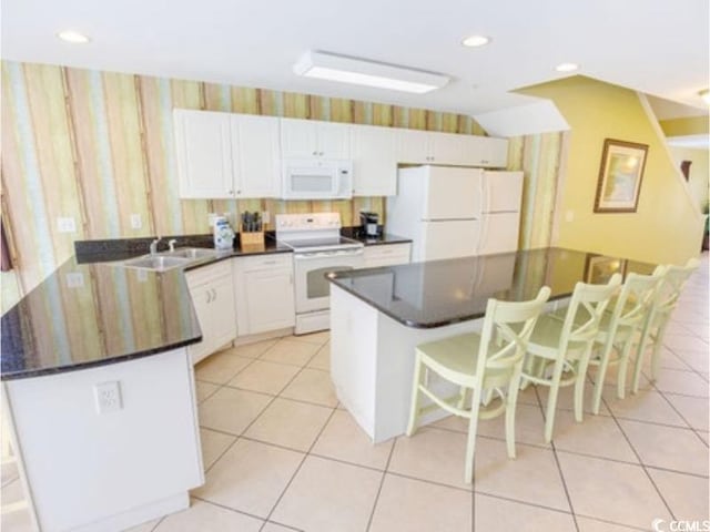 kitchen featuring white appliances, wallpapered walls, white cabinets, dark countertops, and a breakfast bar