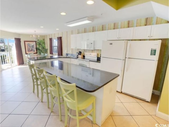 kitchen featuring white appliances, light tile patterned floors, dark countertops, a kitchen breakfast bar, and white cabinetry