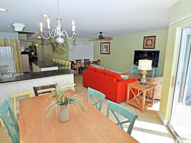 tiled dining room featuring ceiling fan with notable chandelier and a sink