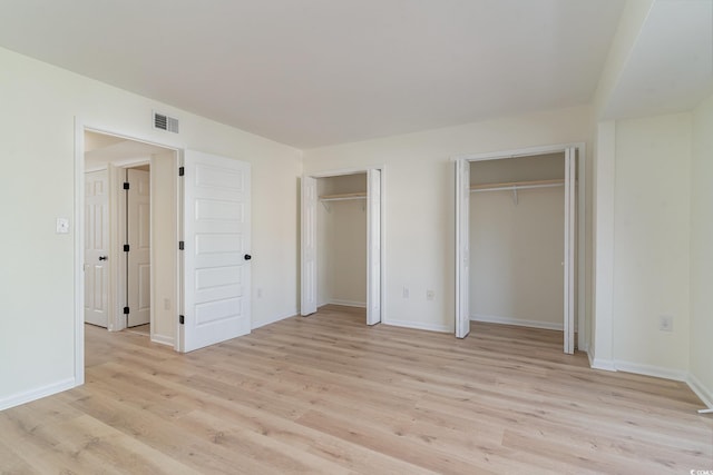 unfurnished bedroom featuring light wood-type flooring and multiple closets