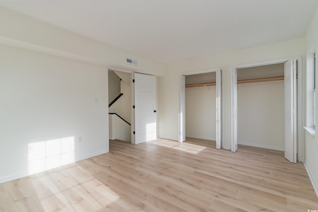 unfurnished bedroom featuring multiple closets and light hardwood / wood-style flooring