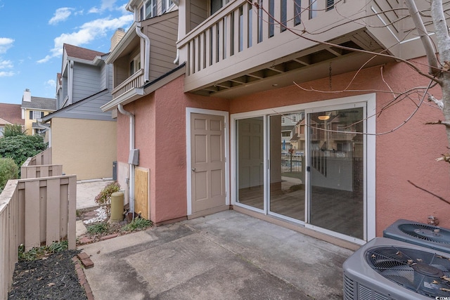 view of exterior entry with central AC, a balcony, and a patio