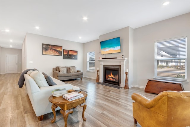 living area with a fireplace with flush hearth, recessed lighting, baseboards, and light wood finished floors