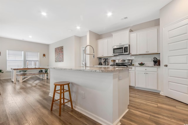 kitchen featuring backsplash, an island with sink, light wood-style flooring, appliances with stainless steel finishes, and a kitchen breakfast bar