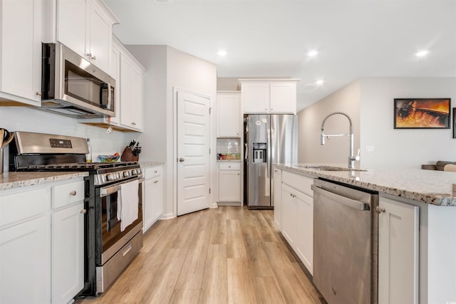 kitchen featuring light wood finished floors, a sink, white cabinets, appliances with stainless steel finishes, and backsplash