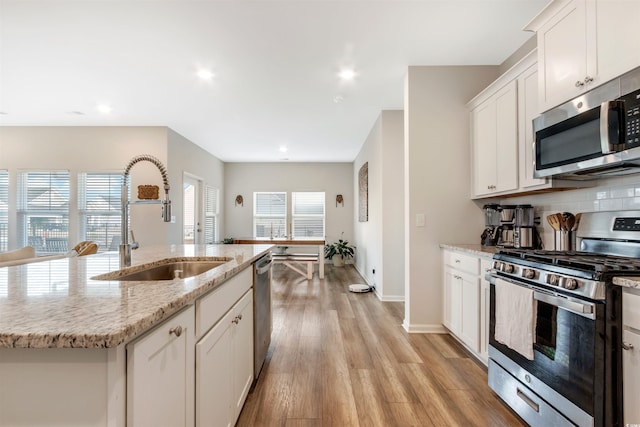 kitchen with decorative backsplash, light wood-style floors, white cabinets, stainless steel appliances, and a sink