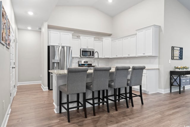 kitchen with light stone countertops, stainless steel appliances, white cabinetry, a breakfast bar area, and an island with sink