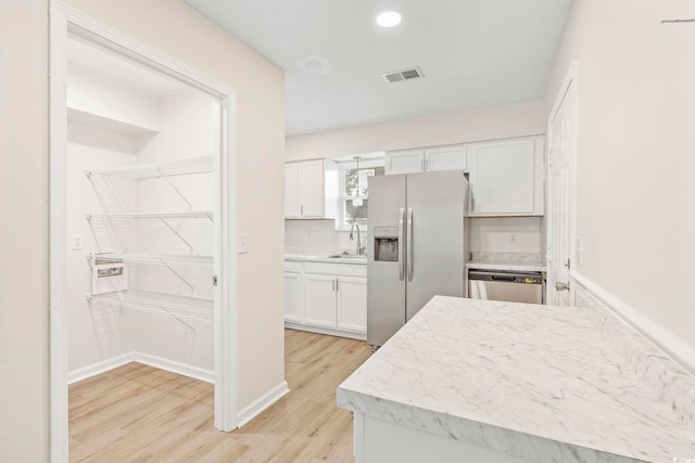 kitchen with sink, tasteful backsplash, light wood-type flooring, appliances with stainless steel finishes, and white cabinets