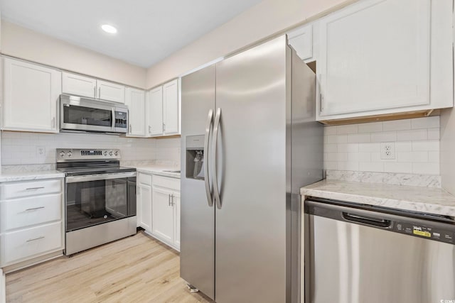 kitchen featuring appliances with stainless steel finishes, light stone countertops, light hardwood / wood-style floors, decorative backsplash, and white cabinets