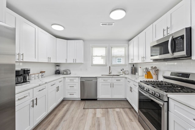 kitchen with appliances with stainless steel finishes, light hardwood / wood-style floors, sink, white cabinetry, and backsplash