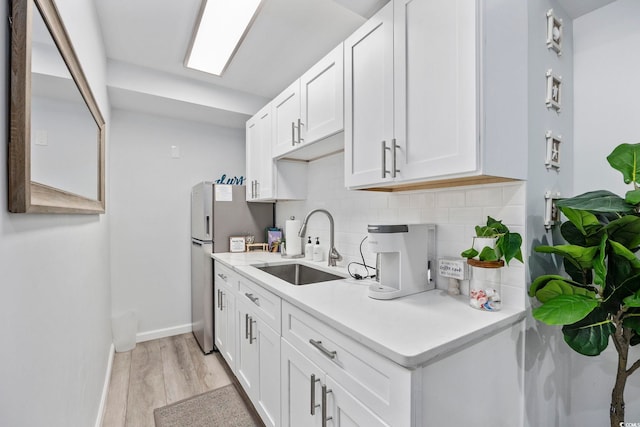 kitchen with sink, white cabinetry, light wood-type flooring, and stainless steel refrigerator