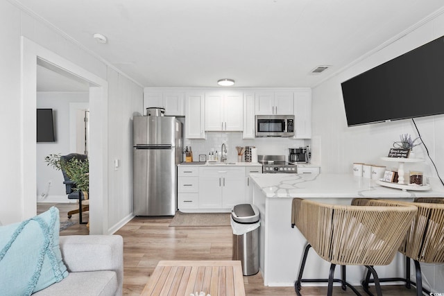 kitchen featuring stainless steel appliances, sink, white cabinetry, a breakfast bar, and crown molding