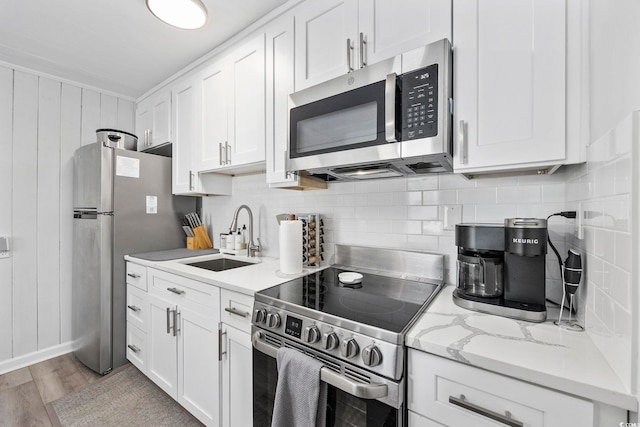 kitchen with stainless steel appliances, sink, white cabinetry, light stone counters, and light wood-type flooring