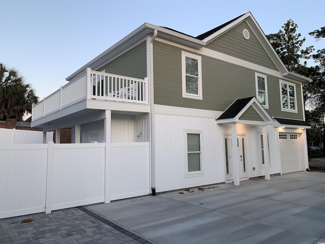 view of front of house featuring concrete driveway, fence, a balcony, and a garage
