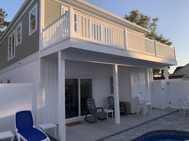 back of house with fence, a fenced in pool, a balcony, and a patio