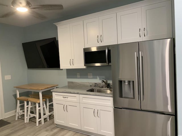 kitchen featuring white cabinets, stainless steel appliances, a sink, light wood-type flooring, and a ceiling fan