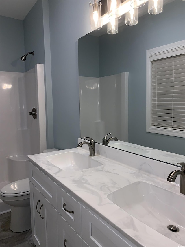 bathroom with double vanity, walk in shower, toilet, and a sink