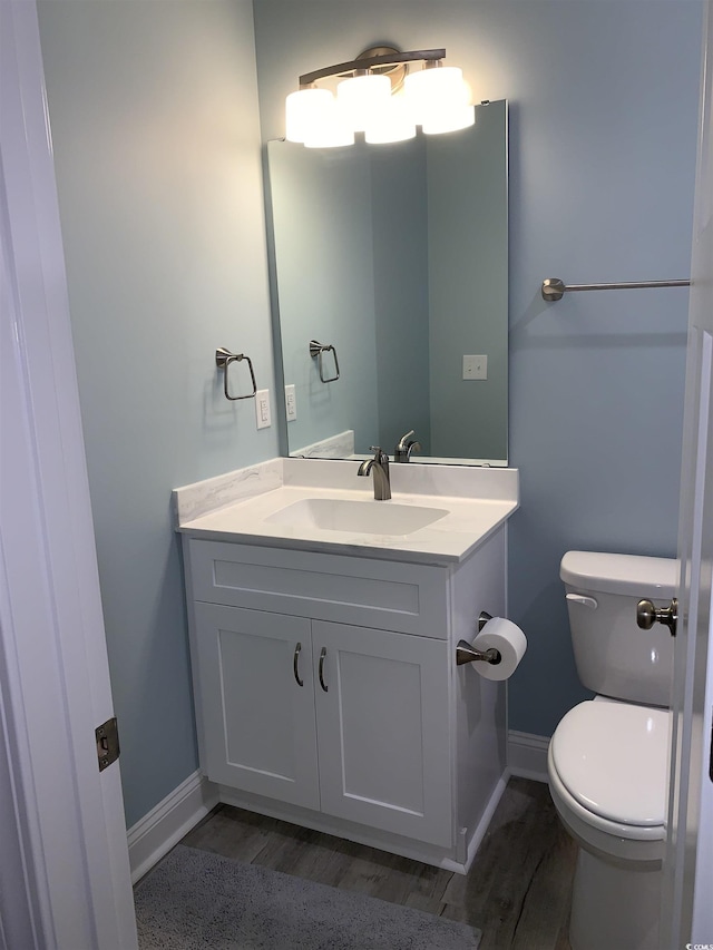 half bathroom featuring wood finished floors, baseboards, vanity, and toilet