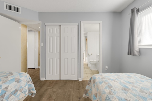 bedroom featuring multiple windows, hardwood / wood-style floors, ensuite bathroom, and a closet