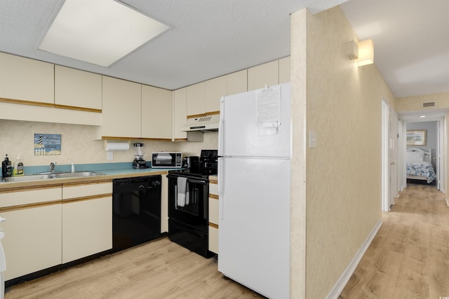 kitchen featuring sink, light hardwood / wood-style floors, a textured ceiling, cream cabinetry, and black appliances