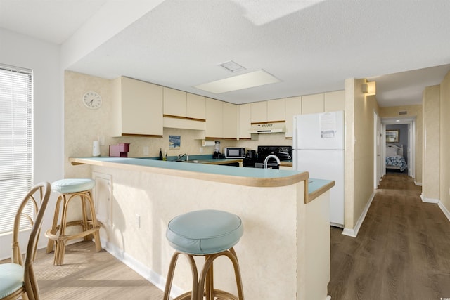 kitchen with a kitchen bar, kitchen peninsula, cream cabinets, and white refrigerator