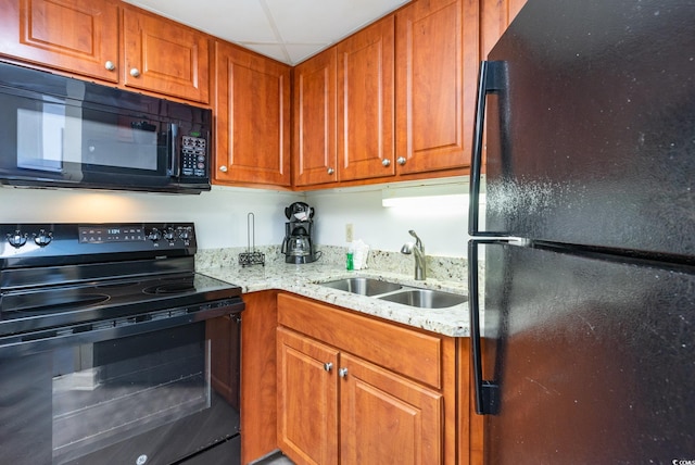 kitchen featuring black appliances, a paneled ceiling, light stone counters, and sink