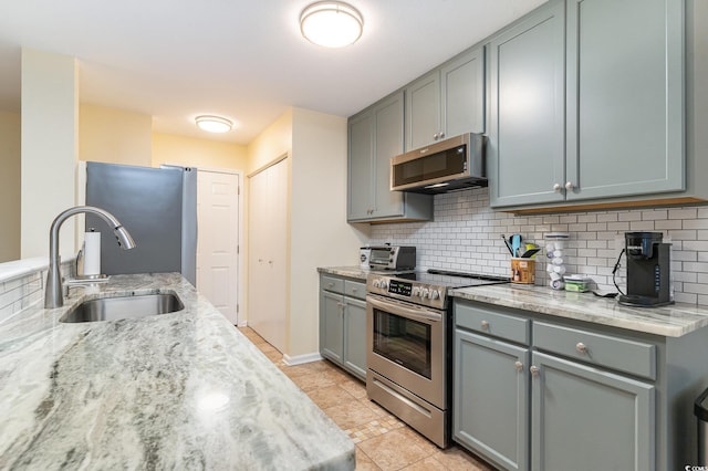 kitchen with sink, decorative backsplash, light stone countertops, light tile patterned floors, and appliances with stainless steel finishes