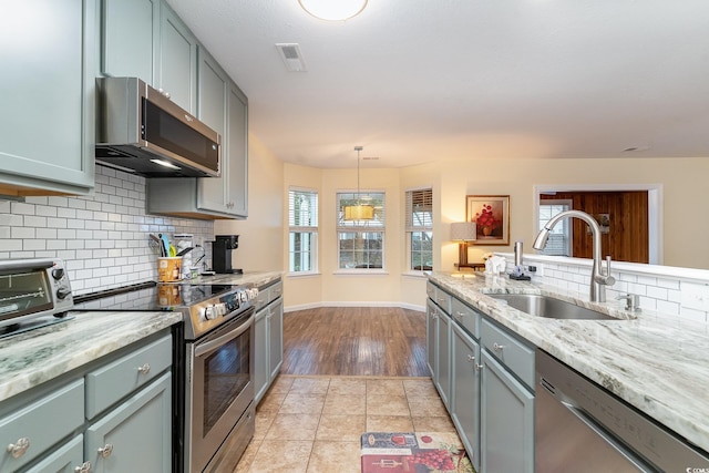 kitchen with light stone countertops, appliances with stainless steel finishes, sink, pendant lighting, and light tile patterned flooring