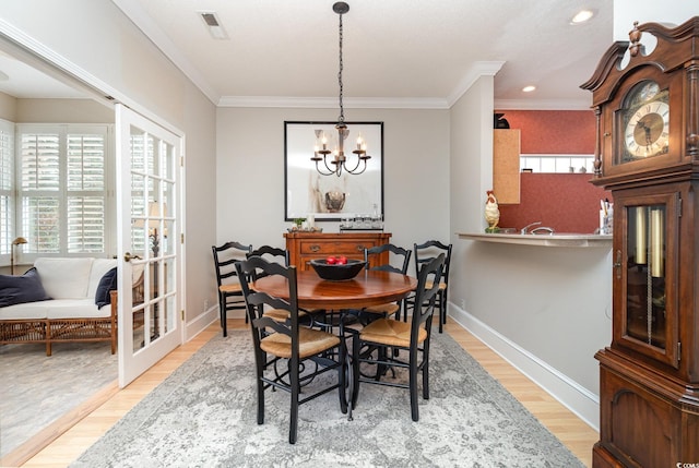 dining area with a notable chandelier, light hardwood / wood-style floors, and crown molding