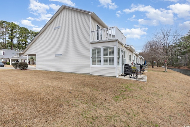 view of side of property featuring a balcony, a patio area, and a lawn