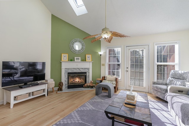 living room with lofted ceiling with skylight, a fireplace, ceiling fan, and light hardwood / wood-style floors