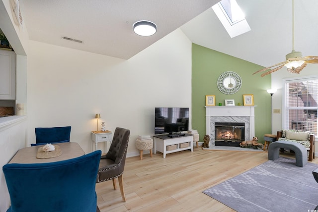 living room featuring a fireplace, light hardwood / wood-style floors, lofted ceiling with skylight, and ceiling fan