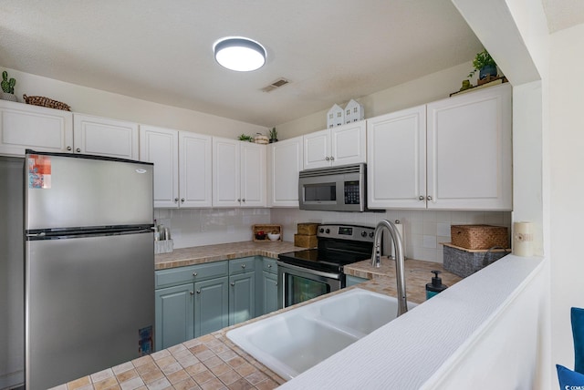 kitchen featuring tile countertops, sink, tasteful backsplash, white cabinetry, and stainless steel appliances