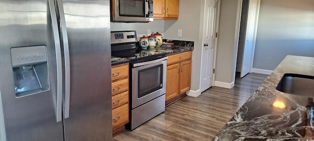 kitchen featuring dark wood-style flooring, brown cabinets, stainless steel appliances, dark countertops, and baseboards