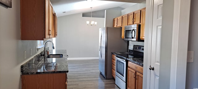 kitchen featuring a sink, appliances with stainless steel finishes, brown cabinets, dark countertops, and pendant lighting