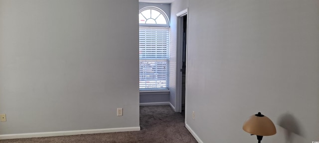 unfurnished room featuring baseboards and dark colored carpet