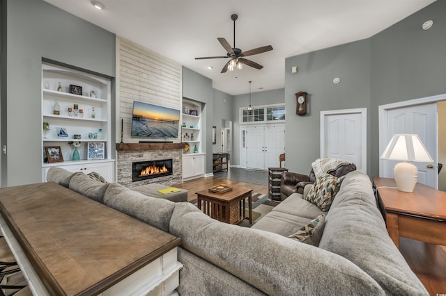 living room featuring hardwood / wood-style flooring, built in features, ceiling fan, and a stone fireplace