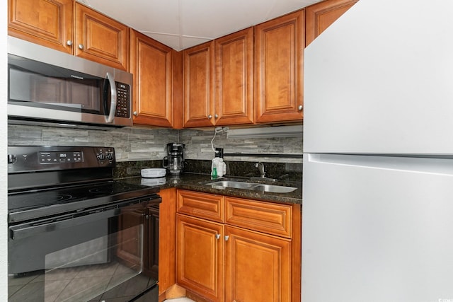 kitchen featuring sink, tasteful backsplash, dark stone countertops, white refrigerator, and black / electric stove