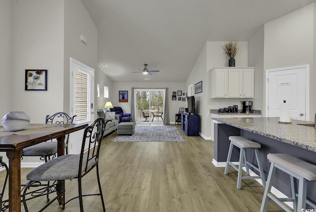 interior space with a kitchen bar, light stone counters, ceiling fan, light hardwood / wood-style flooring, and white cabinetry