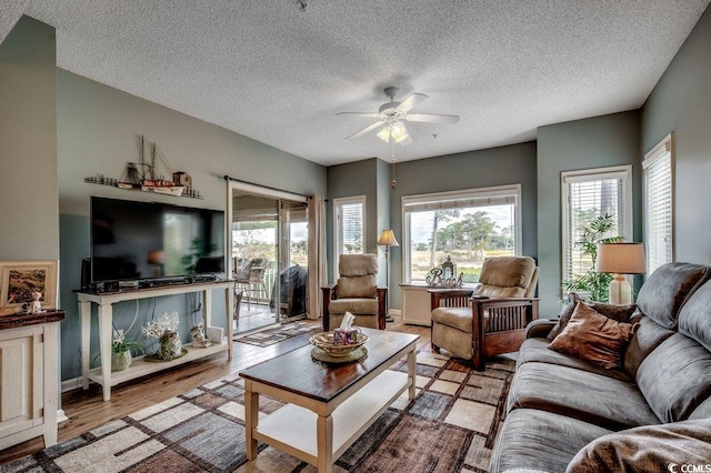 living room with ceiling fan, a textured ceiling, and light wood-type flooring