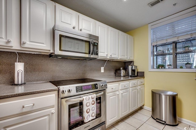 kitchen with backsplash, white cabinets, stainless steel appliances, and light tile patterned floors