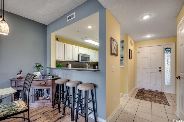 kitchen with a kitchen breakfast bar, light tile patterned flooring, kitchen peninsula, decorative light fixtures, and white cabinets