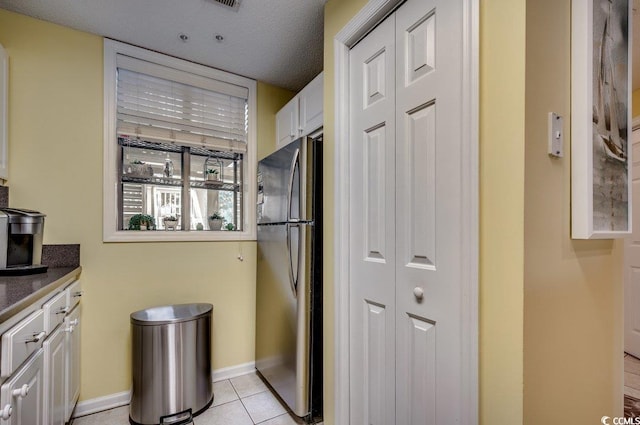 kitchen featuring white cabinets, light tile patterned floors, a textured ceiling, and stainless steel refrigerator