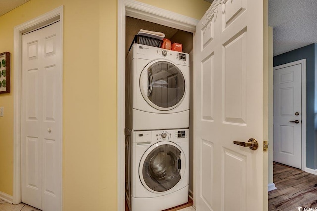 clothes washing area featuring stacked washer / drying machine, light hardwood / wood-style floors, and a textured ceiling