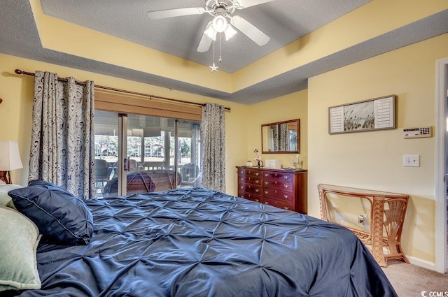 bedroom with access to outside, carpet floors, a tray ceiling, and ceiling fan