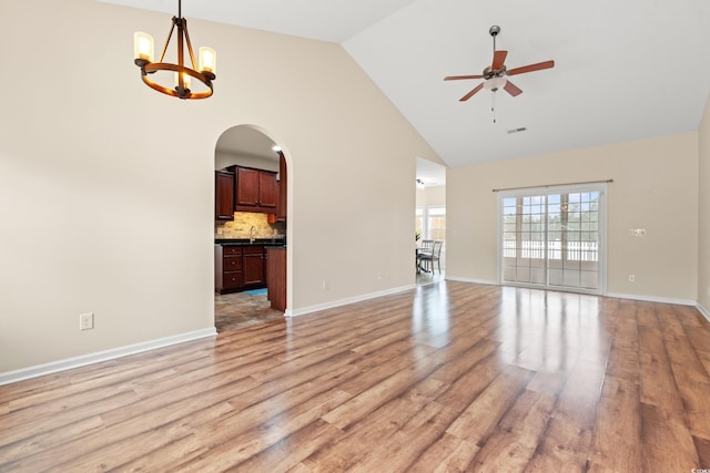 unfurnished living room featuring light wood finished floors, visible vents, arched walkways, high vaulted ceiling, and ceiling fan with notable chandelier