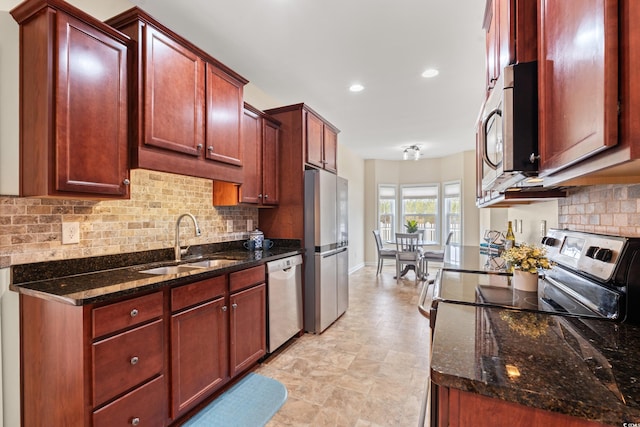 kitchen with reddish brown cabinets, tasteful backsplash, dark stone counters, appliances with stainless steel finishes, and a sink