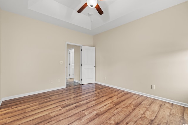 unfurnished room featuring light wood-style floors, a tray ceiling, ceiling fan, and baseboards