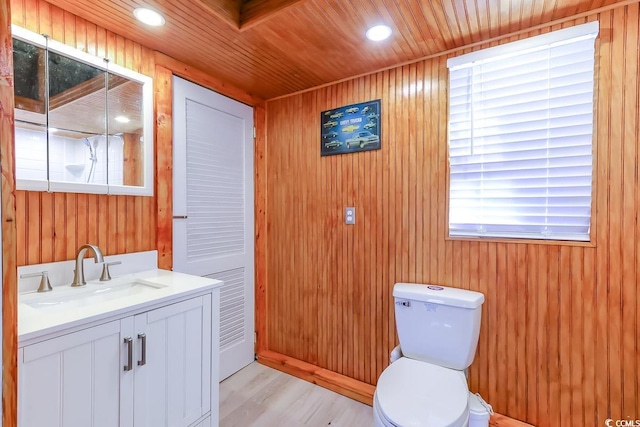 bathroom with hardwood / wood-style flooring, wooden walls, vanity, wooden ceiling, and toilet