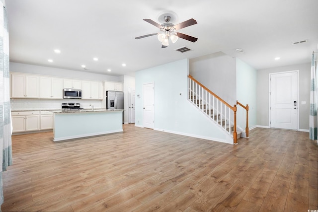 kitchen with backsplash, light wood-type flooring, an island with sink, appliances with stainless steel finishes, and white cabinetry